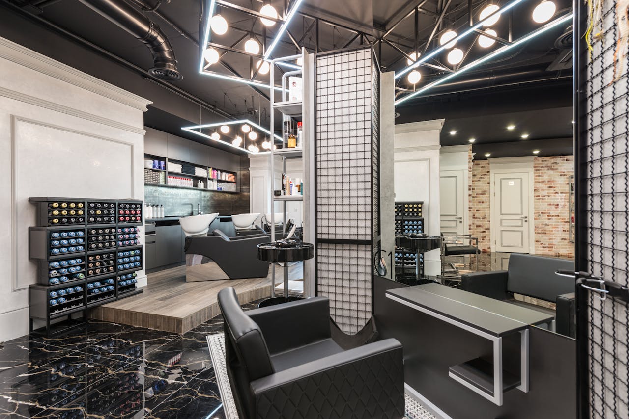 Black leather chair placed against mirror with reflection in stylish beauty salon with backwash chairs and abundance of cosmetology products